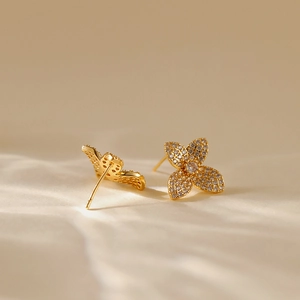 Elegant 18K gold flower leaf earrings with sparkling crystals on textured beige surface