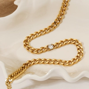 Elegant gold Cuban link necklace with a sparkling white zircon on a ceramic tray