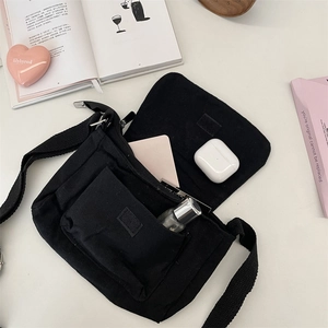 Detail of the black canvas crossbody bag showing velcro flap and multiple storage pockets