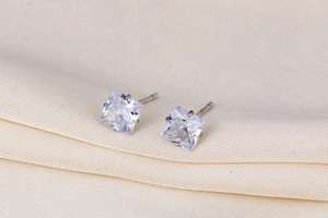 Macro shot of square-cut zircon stud earrings in silver setting on beige fabric background