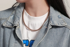 Gros plan d'un collier chaîne serpent en or rose porté par un mannequin en tenue décontractée