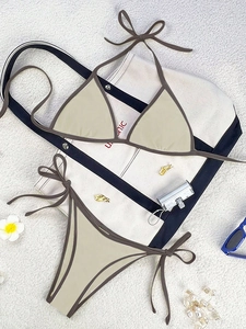 Flat lay of beige bikini set with brown trim alongside beach accessories on sand background