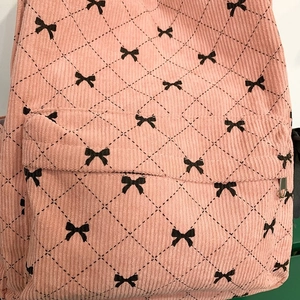 Close-up of pink corduroy school backpack featuring black bows and quilted diamond patterns