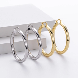 Polished silver and gold large hoop earrings displayed on white geometric stands