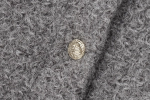 Détail d'un bouton en métal doré texturé sur le tissu gris d'une veste en polaire