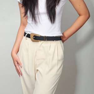 Close-up of women's black leather belt featuring a large irregular gold metal buckle
