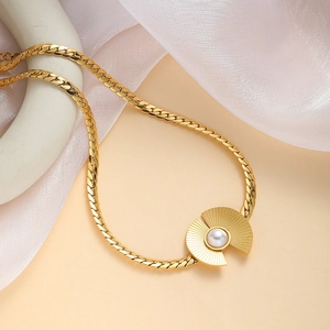 Detailed close-up of golden shell pendant with white pearl on fine snake bone chain