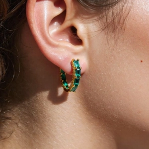 Detailed macro view of 18K gold plated hoop earrings with baguette cut green zircons
