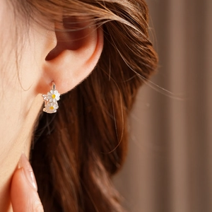 Close-up of vintage silver hoop earrings with white and yellow enamel daisy charms