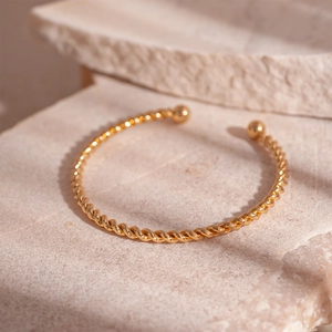 Macro detail of a minimalist twisted gold cuff bracelet with spherical ends on stone