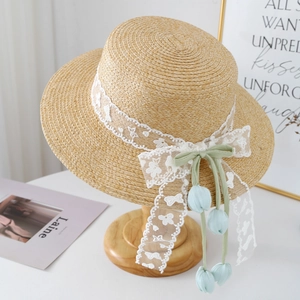 Detail of raffia straw hat with white lace ribbon and blue tulip pendant on wood stand