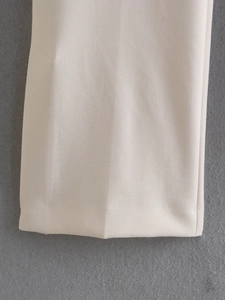 Detailed close-up of beige straight-leg pants showing smooth fabric and split hem stitching