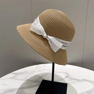 Detail of elegant straw cloche hat featuring a white lace bow and a central pearl accent