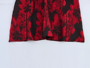 Close-up of elegant black satin maxi dress hem with vibrant red floral jacquard patterns