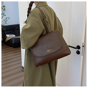 Detail of deep brown PU leather shoulder bag with gold logo and metal chain strap