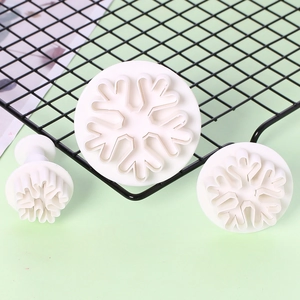 Detailed view of three white plastic snowflake spring plunger cookie cutters on a mesh rack