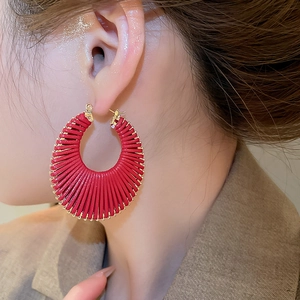 Détail de créoles tressées rouges évidées avec fil métallique doré portées par le mannequin