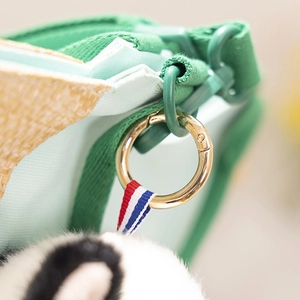 Macro shot of golden spring ring clasp and green strap on a woven straw bag