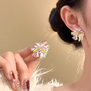 Close-up of colorful firework-shaped stud earrings worn with a soft warm background