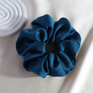 Close-up of a premium blue satin scrunchie resting on soft beige silk fabric background
