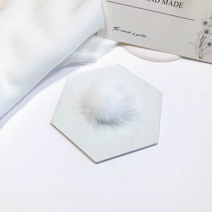 Close-up of a soft white faux mink fur pom-pom on a marble tile for DIY accessories