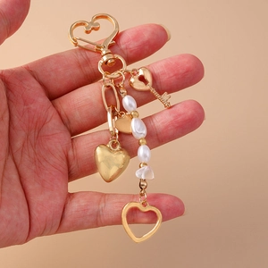 Detalle de llavero de corazón dorado con dijes de llave y tira de perlas blancas