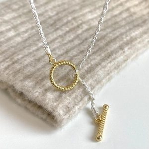 Two-tone silver and gold OT toggle necklace on a soft knit background texture