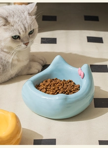 Close-up of a blue ceramic cat bowl with pink bow tie and a white cat in a cozy home setting