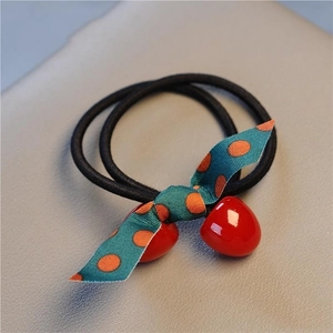 Macro detail of elastic hair tie with blue polka dot bow and glossy red cherry pendants