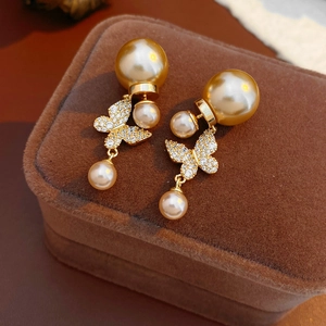 Detailed view of gold butterfly stud earrings with layered pearls on brown velvet