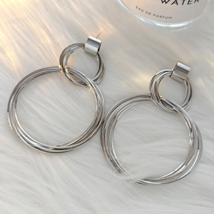 Close-up of double layered silver geometric hoop earrings on a soft white faux fur texture