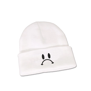 Gros plan détaillé du bonnet en maille blanc avec emoji visage triste brodé en noir