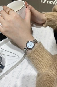 Detail of silver petal-shaped watch with light blue dial on a model wrist with ring