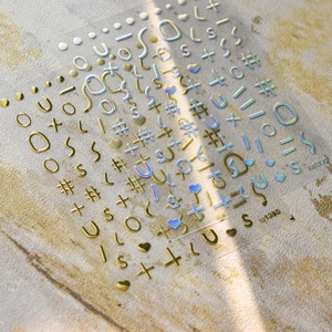 Pegatinas 5D holográficas doradas para uñas con corazones y letras sobre mármol