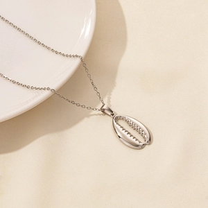 Macro shot of silver seashell pendant with smooth cowrie texture on a textured fabric background