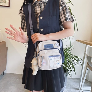 Détail d'un sac bandoulière en toile avec pendentif ourson et autocollants porté par un mannequin