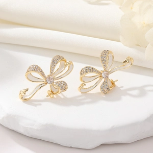 Detail of gold bow earrings with micro-set zircons and white enamel on a stone base