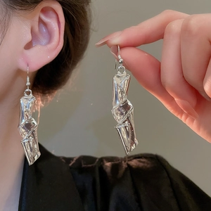 Detail of silver twisted geometric earrings with smooth liquid metal texture on skin