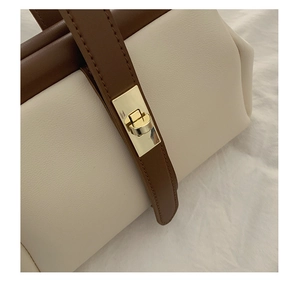 Close-up of contrast leather handbag featuring a polished gold twist lock and fine stitching