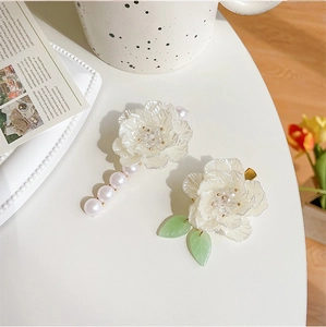 Dettaglio di fermagli per capelli a camelia con perle e foglie verdi su un tavolo