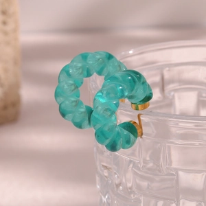Détail de créoles torsadées en acrylique vert translucide sur un bord de verre