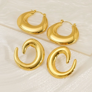 Close-up of golden irregular hoop earrings and C-shaped metal studs on textured background