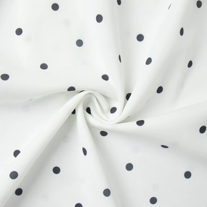 Detailed view of lightweight white chiffon fabric with black polka dots in spiral pleats