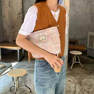Detail of pink floral brocade pouch with a PLEASANT TIME label held by a model