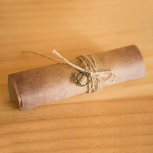 Vintage kraft paper scroll with bronze anchor charm and jute twine on light wood background