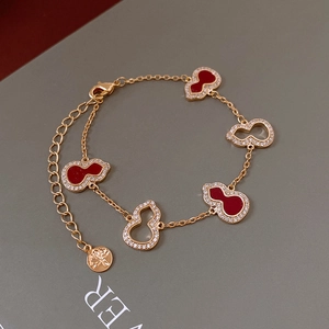 Detail of gold chain bracelet with red and hollow wulu charms on green gift box