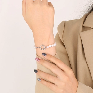 Détail d'un bracelet de perles blanches avec fermoir OT argenté sur le poignet d'un mannequin
