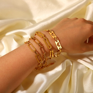 Close-up of four layered 18K gold stainless steel chain bracelets on a silk background