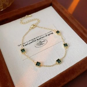 Gros plan d'un bracelet doré avec cinq zircons verts carrés sur un coussin de velours