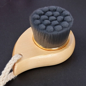 Detail of wooden facial brush with soft wavy bristles and a gold ring connector